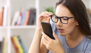 Girl wearing eyeglasses with eyesight problems trying to read phone text at home